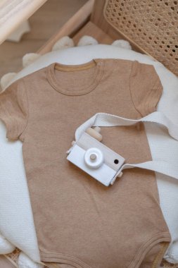 Flat lay composition bodysuit and wooden camera.Baby clothes and accessories set on neutral beige background. Fashion Scandinavian children's clothes