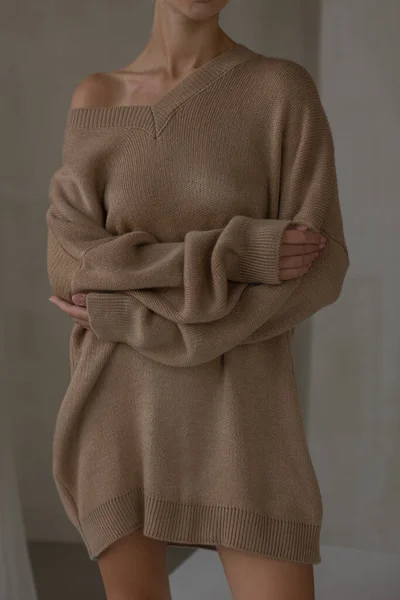 cozy aesthetics. girl hugs herself, dressed in brown, large-knit sweater. no face.