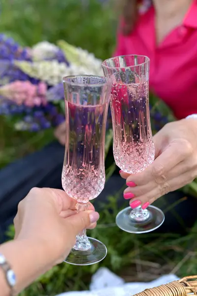 Girls\' hands hold crystal glasses with pink wine, meeting friends, celebration, garden, lupin, spring, picnic, selective focus, background