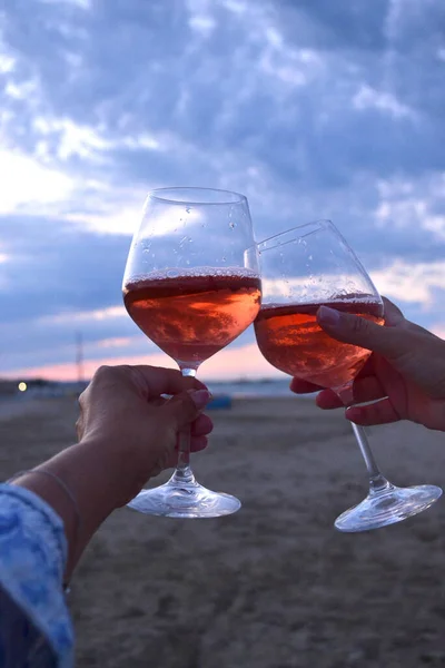 Glasses with pink wine on the background of a sunset at sea. Glasses in his hands, without a face. Beautiful background. Vacation with friends. Italy. Selective focus.