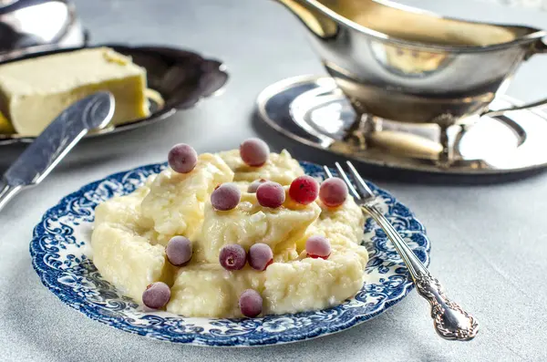 Lazy dumplings with cottage cheese on a blue plate, served with hot butter, sugar and frozen red berries, knife. silver fork and saucer, homemade food, traditional Ukrainian cuisine