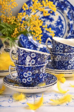 Mavi porselen bardaklar ve çiçekli mimozalar, beyaz masa örtüsü, anneler günü, güzel bir ortam, bahar, arka plan.