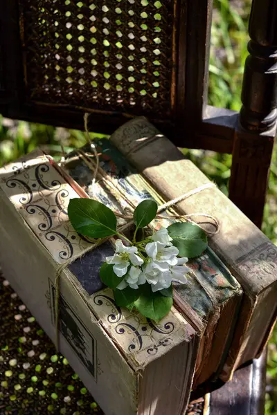 A stack of old books on a chair in the garden, a sunny spring day, a sprig of a flowering apple tree, an antique chair, reading books, selective focus, background