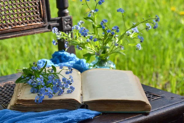 An open book on a chair in the garden, pages without text, copy space, an old book, a bouquet of forget-me-nots, relaxation, rest in the garden, weekend, summer, vacation, reading books.