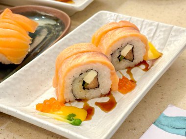 Somon balıklı suşi ve beyaz tabakta avokado.