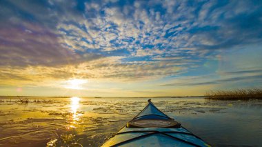 Göl kıyısındaki mavi kanonun pruvasından kışın veya ilkbaharın başlarında buatif günbatımında buz kütleleri ile görüntülenir. Kış kanosu