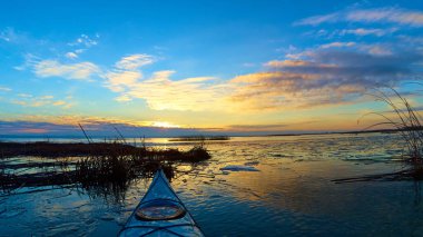 Göl kıyısındaki mavi kanonun pruvasından kışın veya ilkbaharın başlarında buatif günbatımında buz kütleleri ile görüntülenir. Kış kanosu