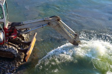 Bir kazıcı gölün dibini derinleştiriyor zemini aşağıdan kamyona yüklüyor.