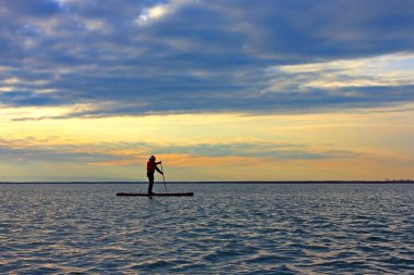 Durgun kış akşamında sakin gölde günbatımında kürek çeken kürekçinin silueti.