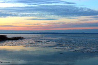 Suda yüzen buz kütleleriyle berrak, sakin bir göl. Mavi akşam ışığı ve mor bulutlu gökyüzü Kış nehri veya gölde