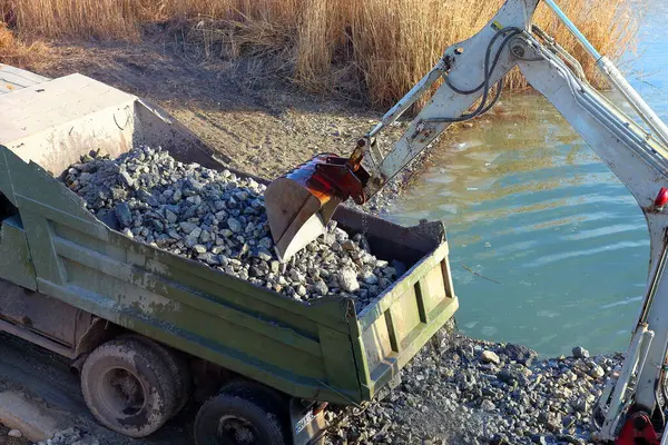 Bir kazıcı gölün dibini derinleştiriyor zemini aşağıdan kamyona yüklüyor.