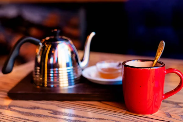 Red cup, metal kettle on a wooden dark table. Tea party in the restaurant. High quality photo