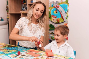 Anne ve oğlu masaya oturup kağıt ve yapıştırıcıdan bir şeyler yapıyorlar. Yaratıcı ders, el yapımı. Yüksek kalite fotoğraf