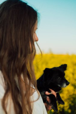 A pregnant woman with a small black dog in nature. Rapeseed field. High quality photo