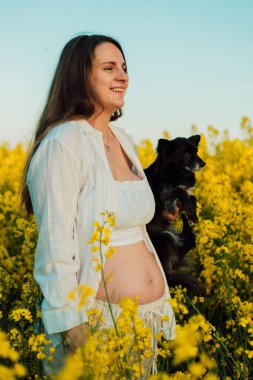 A pregnant woman with a small black dog in nature. Rapeseed field. High quality photo