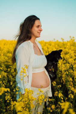 A pregnant woman with a small black dog in nature. Rapeseed field. High quality photo