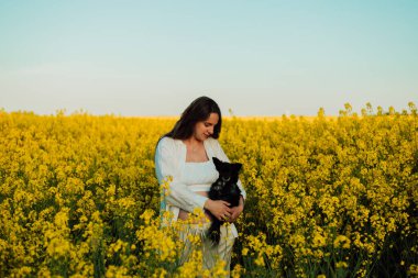 A pregnant woman with a small black dog in nature. Rapeseed field. High quality photo