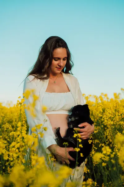 A pregnant woman with a small black dog in nature. Rapeseed field. High quality photo