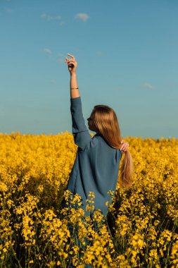 Kolza tohumu tarlasında duran güzel genç bir kadın. Mavi gökyüzüne karşı tecavüz tarlası. Yüksek kalite fotoğraf