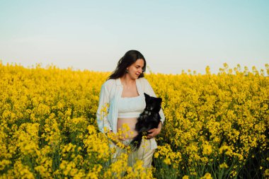 A pregnant woman with a small black dog in nature. Rapeseed field. High quality photo