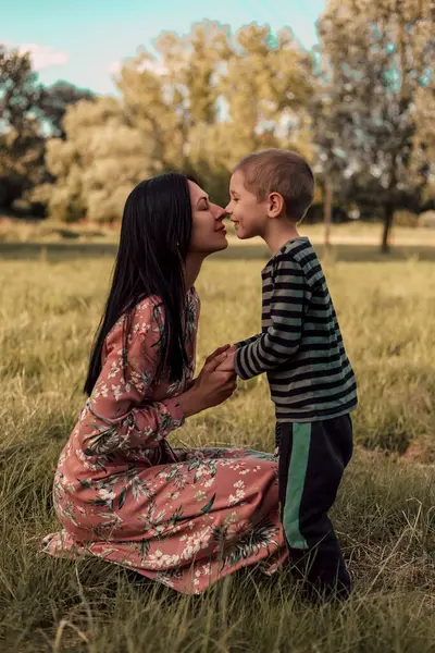 Mother and son touch their noses to each other. Mom squatted down. They are happy. Mother and son in nature look at each other. A family day in the park for a walk. High quality photo