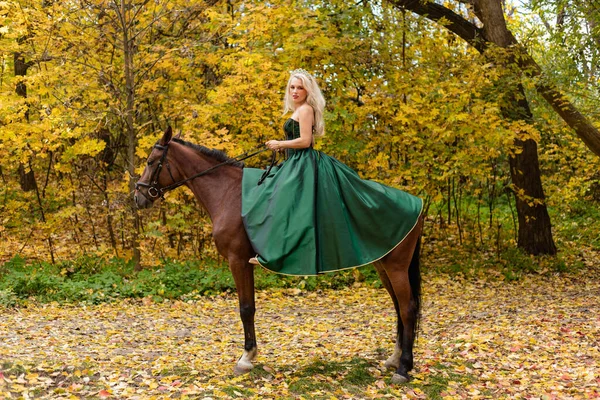 A woman in a long dress sits on a horse. Autumn forest, horse breeding. High quality photo