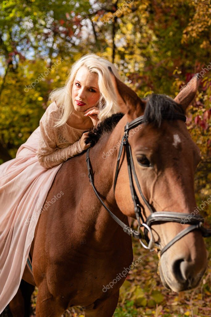 Una mujer con un vestido largo se sienta en un caballo. Bosque de otoño