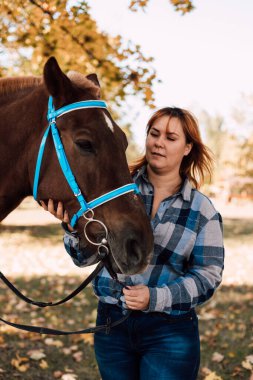 Bir kadın atı dizginlerinden tutar. Sonbahar ormanında ata binmek. At kiralama. Yüksek kalite fotoğraf