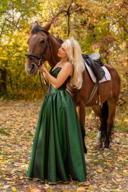 Uzun elbiseli bir kadın ata biner. Sonbahar ormanı, at yetiştiriciliği. Yüksek kalite fotoğraf