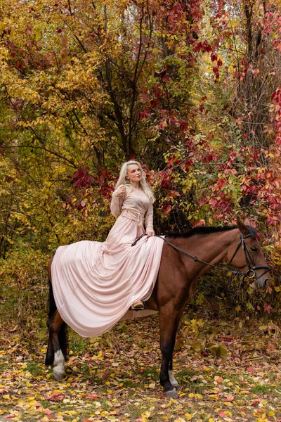 Uzun elbiseli bir kadın ata biner. Sonbahar ormanı, at yetiştiriciliği. Yüksek kalite fotoğraf