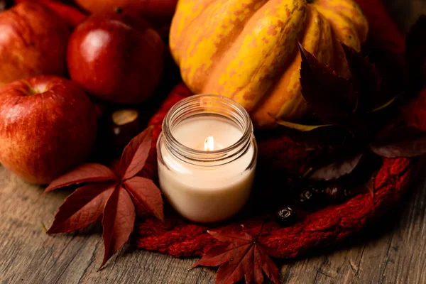 Burning candle on the table next to apples and grape leaves. Autumn Composition. High quality photo
