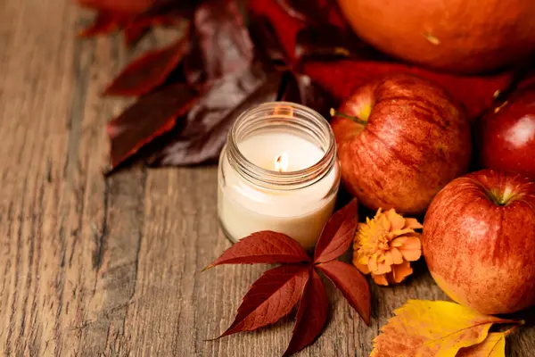 Burning candle on the table next to apples and grape leaves. Autumn Composition. High quality photo