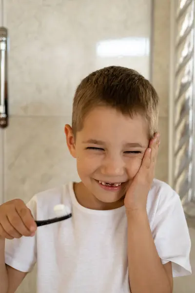Little boy in white t-shirt brushing his teeth in the bathroom. Milk teeth are replaced by molars. High quality photo
