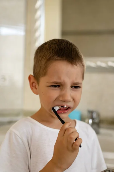 Little boy in white t-shirt brushing his teeth in the bathroom. Milk teeth are replaced by molars. High quality photo