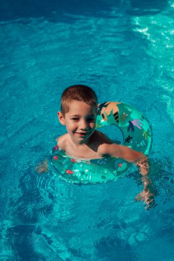 Çemberli küçük bir çocuk berrak mavi suda banyo yapıyor. Havuzda yüzmek. Yüksek kalite fotoğraf