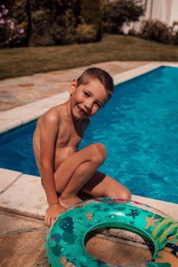 Küçük bir çocuk havuzun yanında oturuyor. Yaz sıcağında güneş yanığı, öğlen. Yüksek kalite fotoğraf