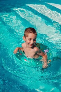 Çemberli küçük bir çocuk berrak mavi suda banyo yapıyor. Havuzda yüzmek. Yüksek kalite fotoğraf