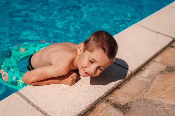 A little boy climbs out of the pool. A child bathes at noon in the heat. High quality photo