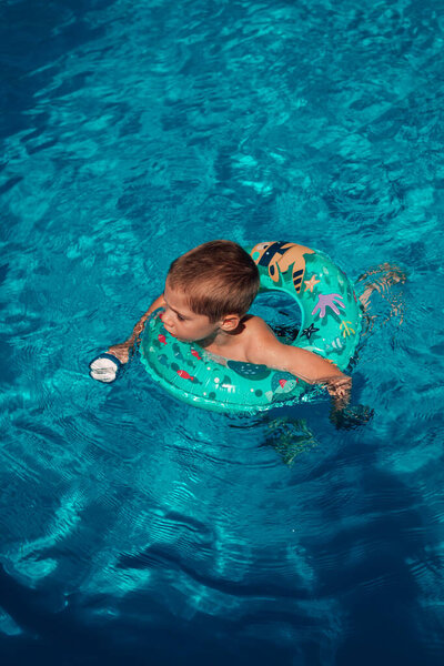 Ребенок плавает один в бассейне с спасательным буем. Чистая чистая вода. Вид сверху. Высокое качество фото