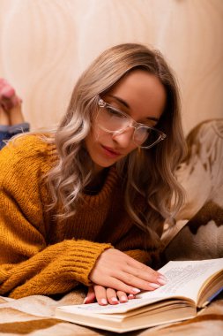 Kanepede kitabı olan bir kadın. Bir kadın kitap okuyor. Evde öğreniyorum. Yüksek kalite fotoğraf