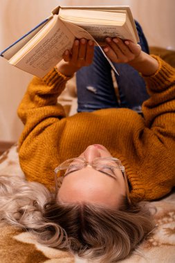 Kanepede kitabı olan bir kadın. Bir kadın kitap okuyor. Evde öğreniyorum. Yüksek kalite fotoğraf
