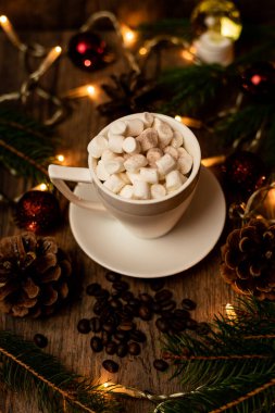 Noel ışıklarıyla dolu bir masada beyaz bir fincanda marşmelov. Noel ağacı ve koniler masanın üstünde. Yüksek kalite fotoğraf