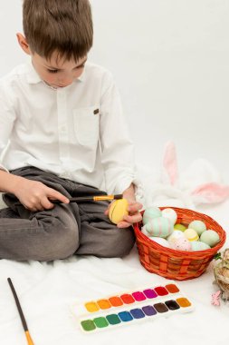 Paskalya Tavşanı Kulaklı Küçük Çocuk, Beyaz Arkaplanda Paskalya Yumurtası Boyuyor. Yüksek kalite fotoğraf