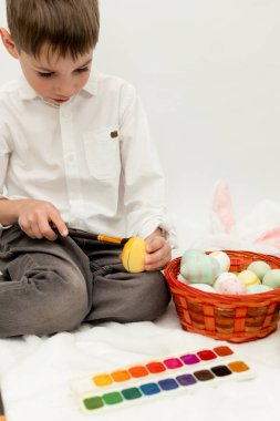 Paskalya Tavşanı Kulaklı Küçük Çocuk, Beyaz Arkaplanda Paskalya Yumurtası Boyuyor. Yüksek kalite fotoğraf