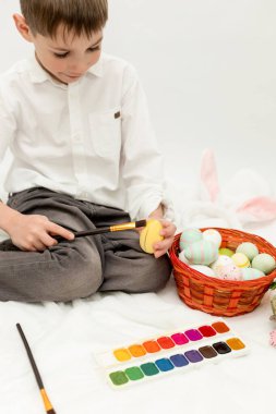 Paskalya Tavşanı Kulaklı Küçük Çocuk, Beyaz Arkaplanda Paskalya Yumurtası Boyuyor. Yüksek kalite fotoğraf