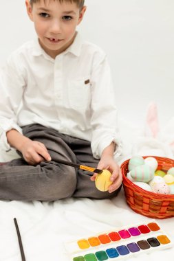Paskalya Tavşanı Kulaklı Küçük Çocuk, Beyaz Arkaplanda Paskalya Yumurtası Boyuyor. Yüksek kalite fotoğraf