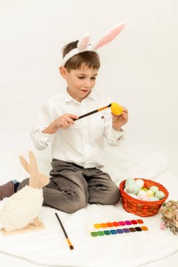 Paskalya Tavşanı Kulaklı Küçük Çocuk, Beyaz Arkaplanda Paskalya Yumurtası Boyuyor. Yüksek kalite fotoğraf