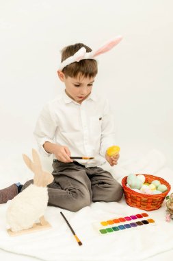 Paskalya Tavşanı Kulaklı Küçük Çocuk, Beyaz Arkaplanda Paskalya Yumurtası Boyuyor. Yüksek kalite fotoğraf