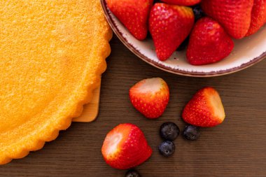 Masanın üzerinde sünger kek var. Çilekli turta yapma süreci. Masada çilek ve yaban mersini var. Yüksek kalite fotoğraf