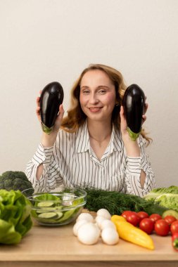 Masada elinde patlıcan olan bir kadın. Masada taze sebzeler var. Vejetaryen yemeği. Yüksek kalite fotoğraf